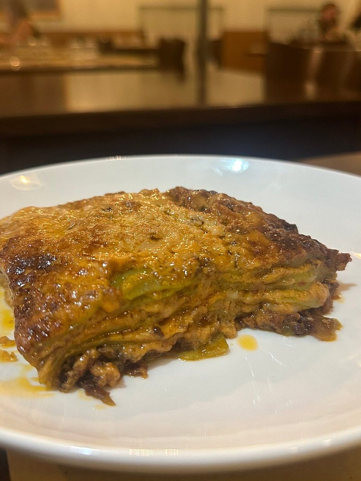 Phone photo of a lasagna slice in flat light, layers blurred together and the cheese top looking pale and greasy