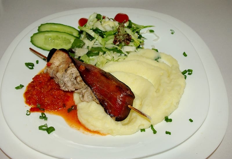 Bacon-wrapped pork skewer with mashed potato and ajvar, relit with PlateRefresh — unedited phone photo